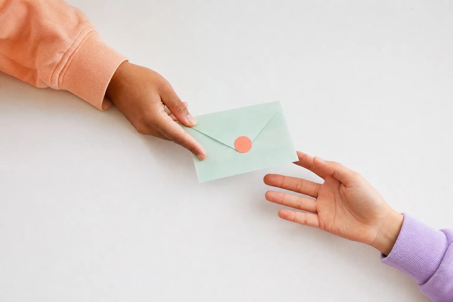One hand passing a sealed mint-green envelope to another